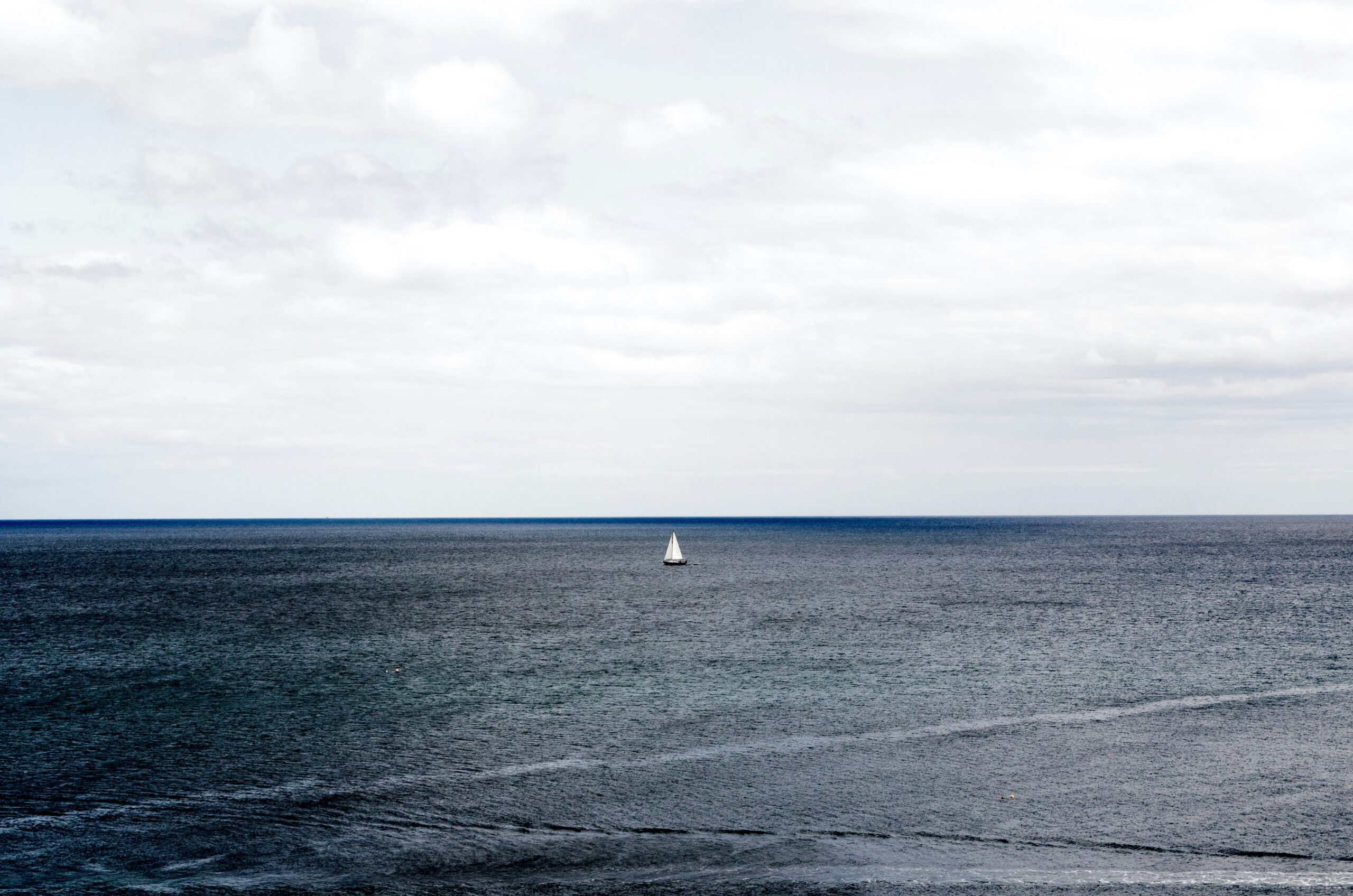white sailboat on ocean under cloudy sky during daytime